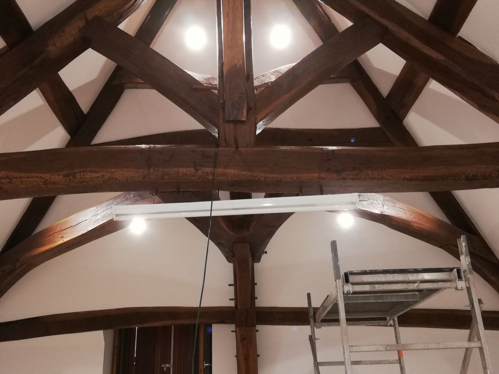 Poutres de plafond voûtées en bois avec éclairage et échafaudage dans un espace intérieur.