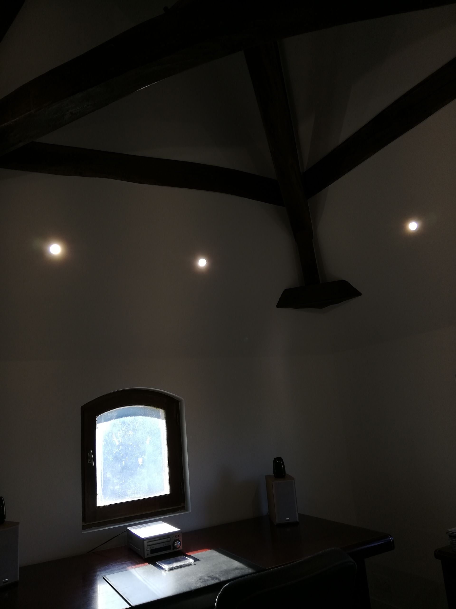 Pièce sombre avec un bureau et une fenêtre lumineuse, éclairée par de petites appliques murales.