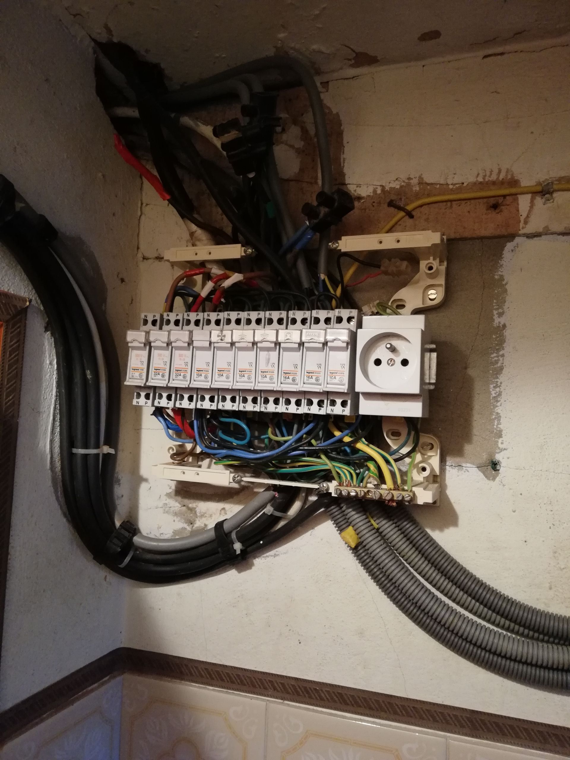 Tableau électrique encastré dans un mur, avec fils et conduits apparents.