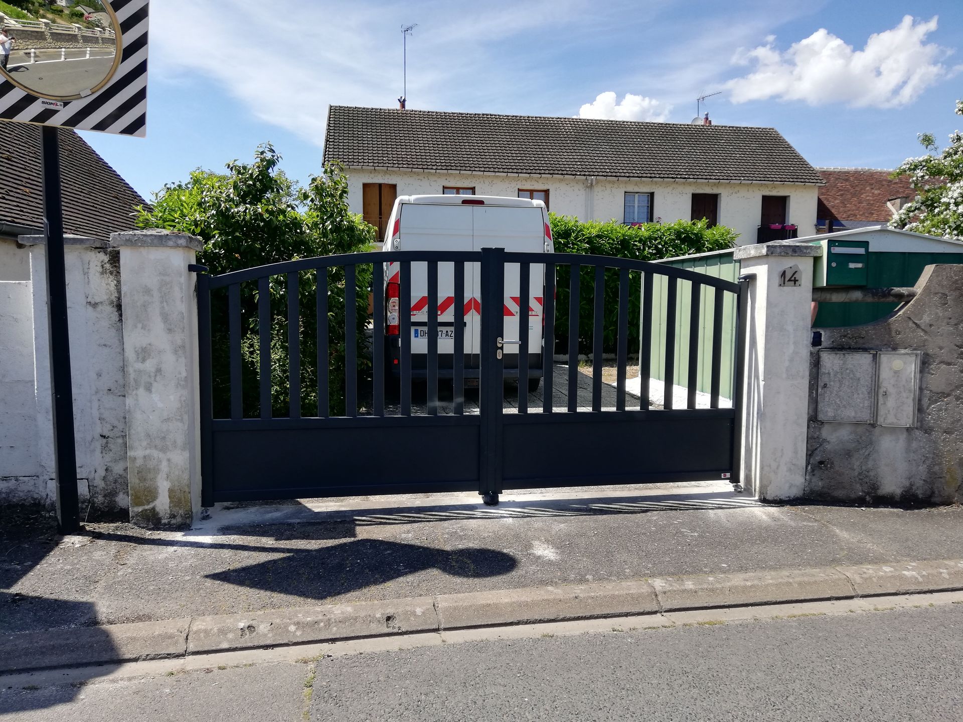 Maison avec portail noir motorisé et piliers blancs.