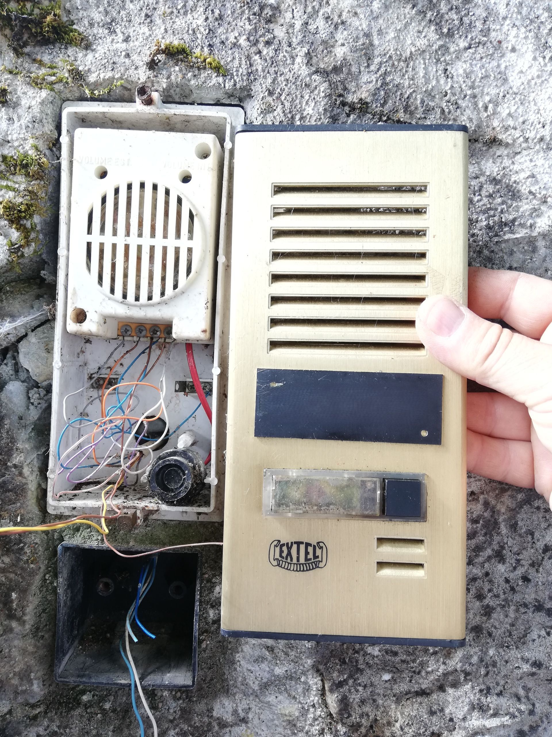 Un interphone avec grille de haut-parleur et boutons, partiellement ouvert.