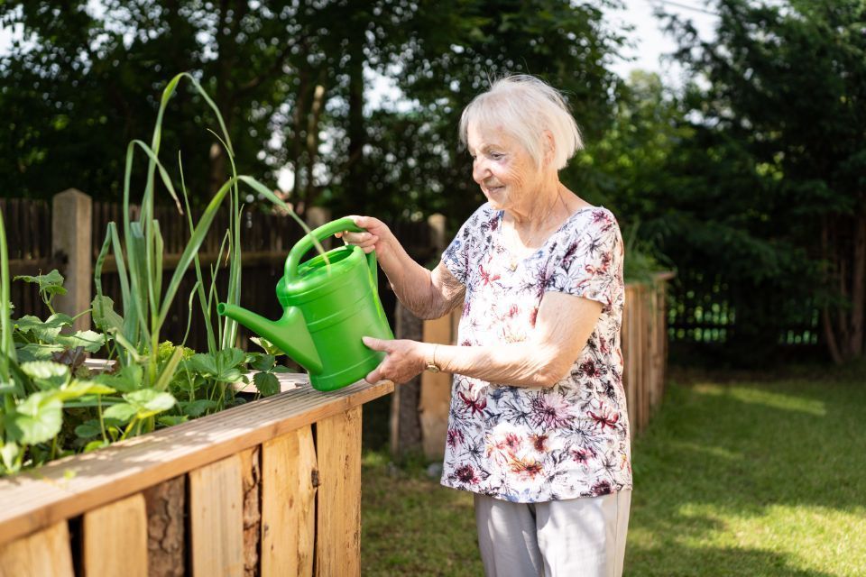 Bewohnerin der Senioren-Wohngruppe von Ambulanter Pflegedienst Floß gießt Blumen im Garten