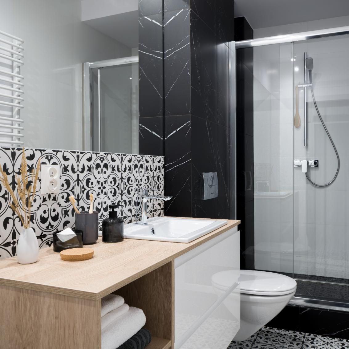 Baño moderno con azulejos estampados, tocador de madera, espejo y ducha de cristal con grifería cromada.