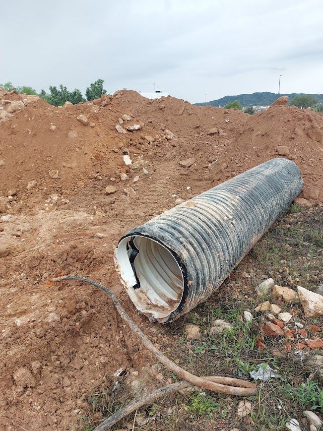 Tubo corrugado roto yace junto a un gran montón de tierra en una obra de construcción.