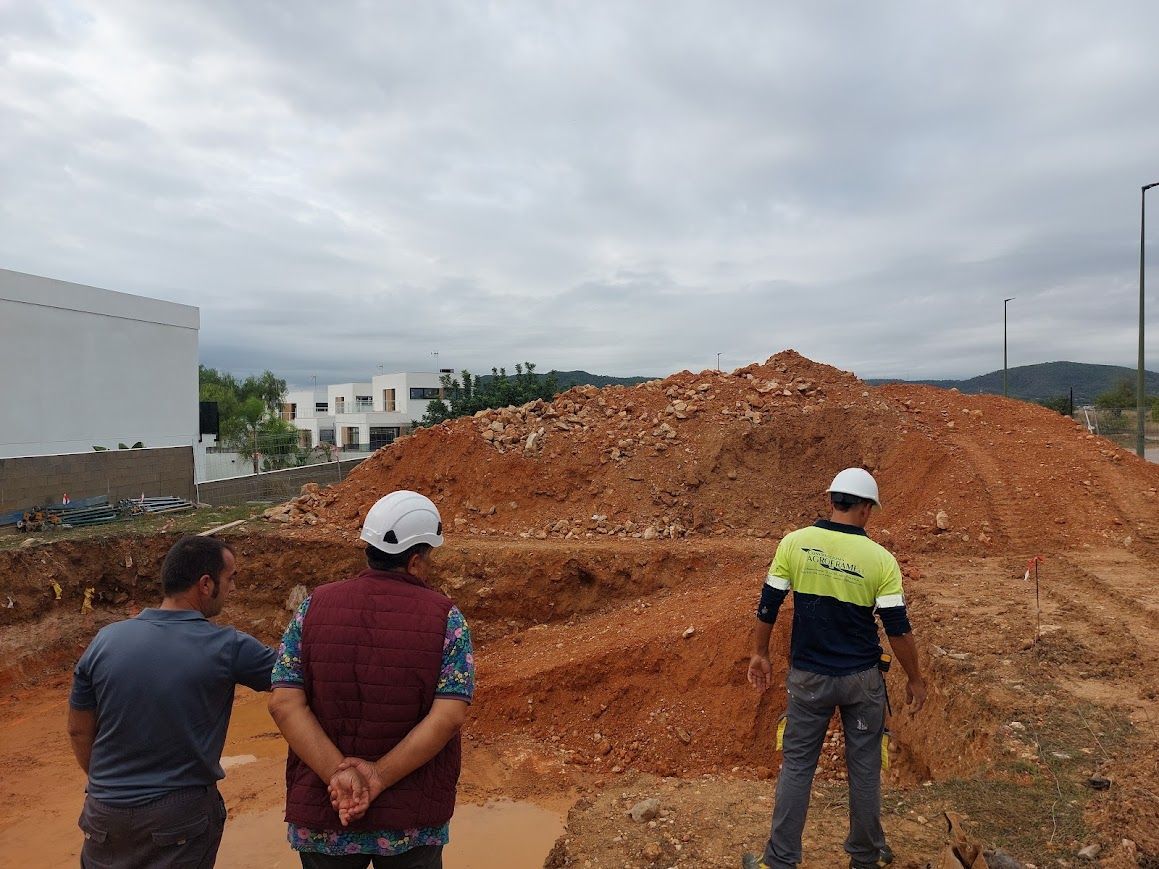 Tres trabajadores con cascos inspeccionan un gran montículo de tierra en una obra de construcción.
