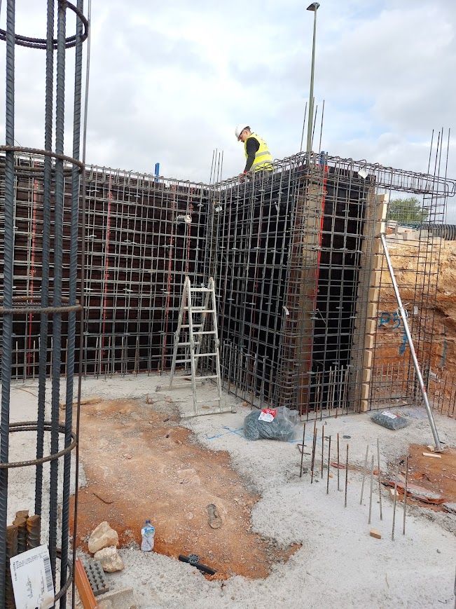 Obrero de la construcción sobre andamios y barras de refuerzo en una obra de cimentación de hormigón.