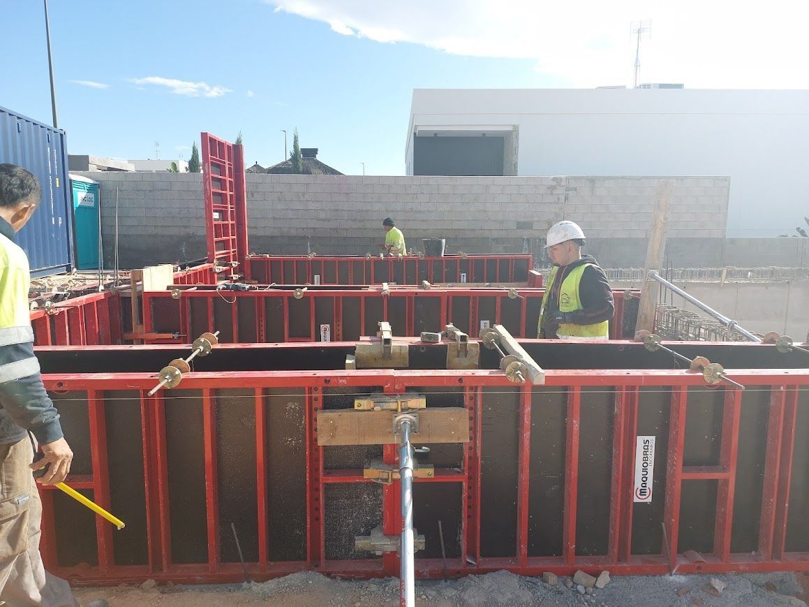 Obreros de la construcción cerca de un gran foso de encofrado rojo en una obra bajo la luz del día.