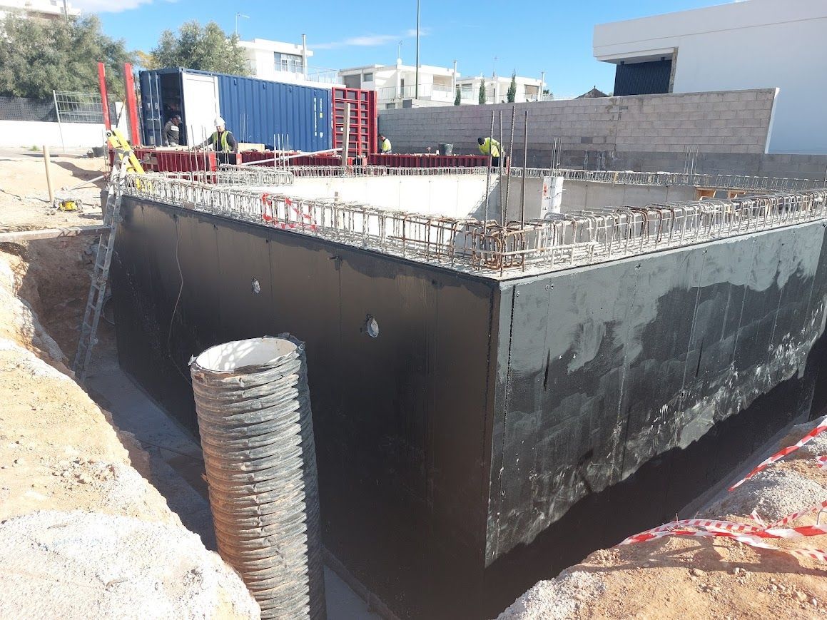 Obra en construcción con una gran base de hormigón, barras de refuerzo que sobresalen y un muro 