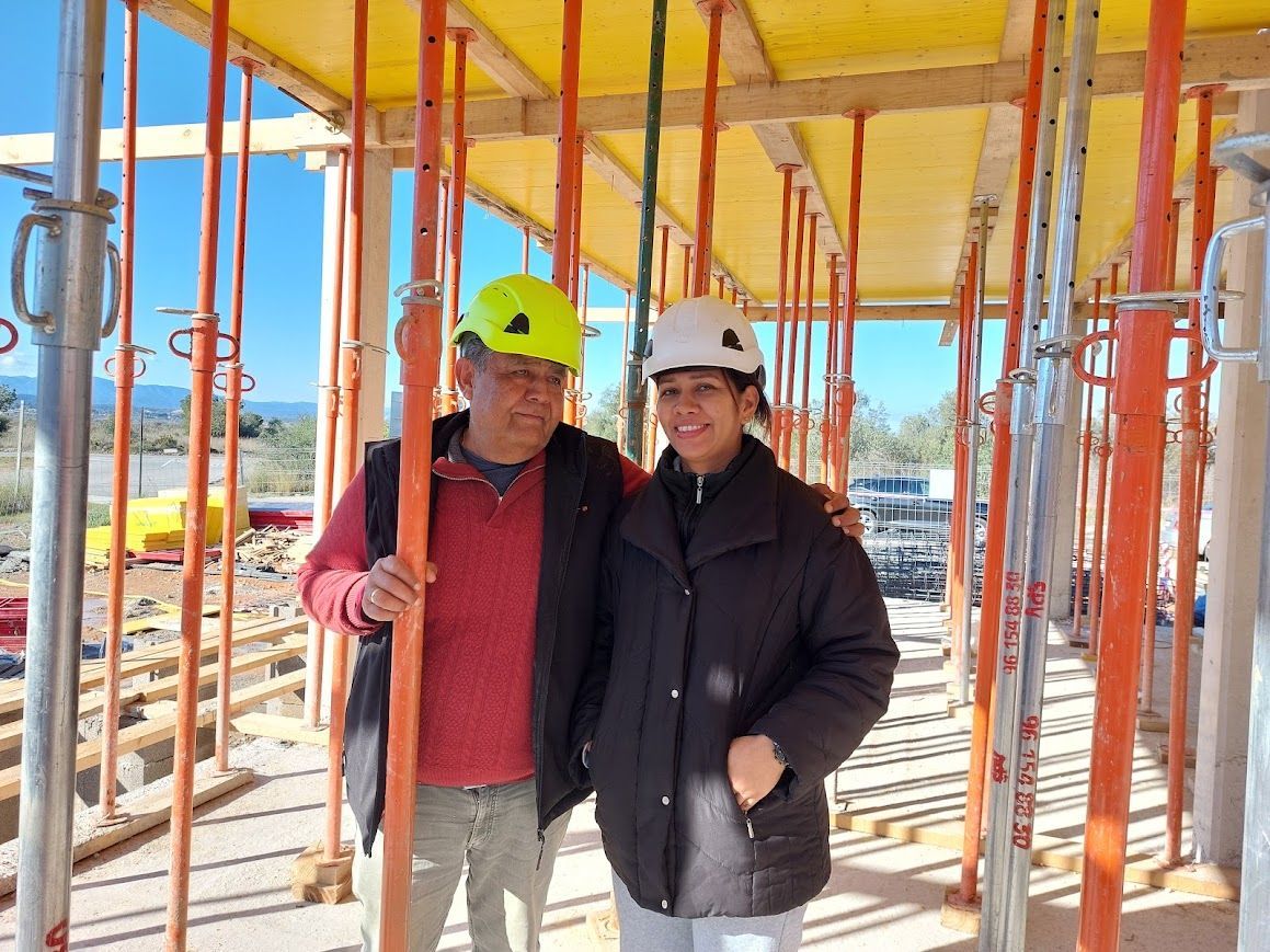 Dos personas con cascos de seguridad se encuentran en una obra en construcción bajo un andamio.