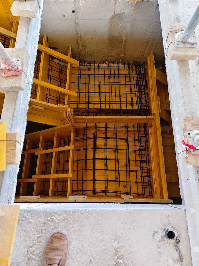 Vista desde arriba de un pozo de hormigón con encofrado amarillo y barras de refuerzo dentro de una obra en construcción.