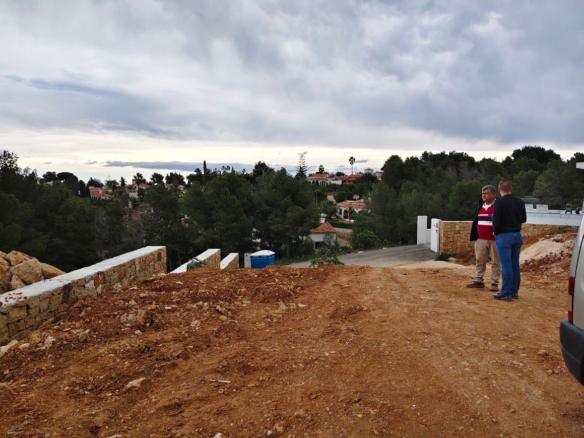 Mirador de un camino de tierra con dos personas de pie cerca de una zona boscosa bajo un cielo nublado.