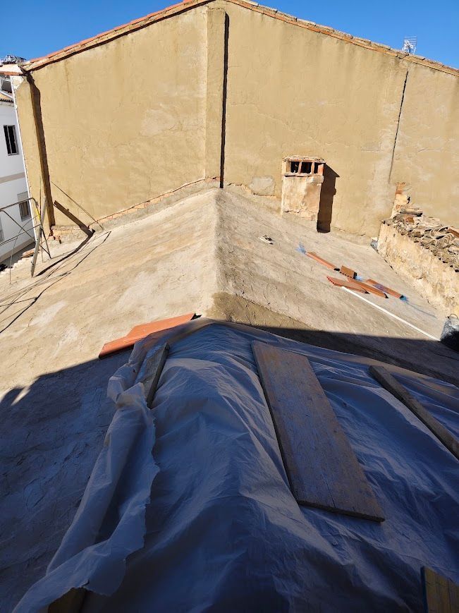 Azotea con lonas en primer plano, paredes de estuco beige y una pequeña chimenea o conducto de ventilación 