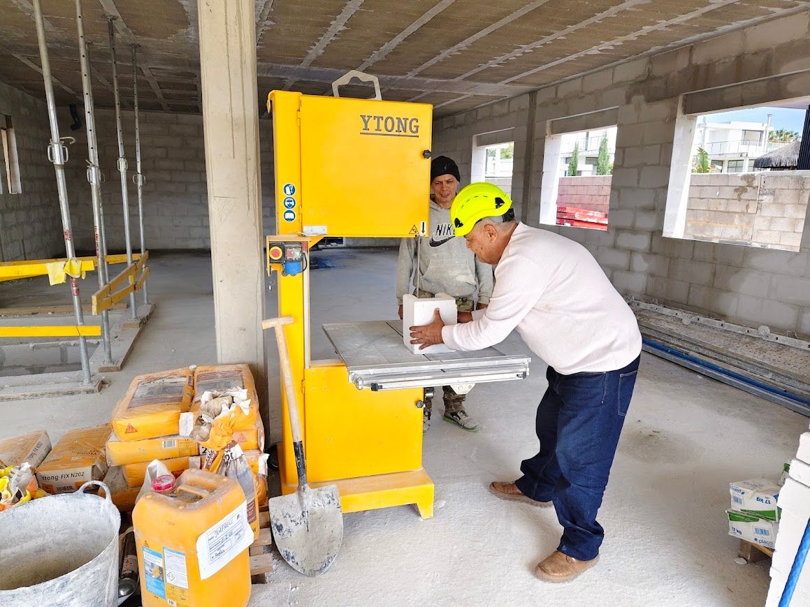Trabajadores utilizando una plataforma elevadora amarilla dentro de un edificio sin terminar con herramientas