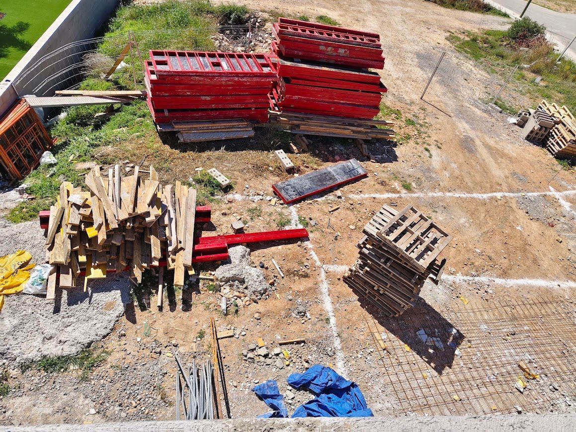 Obra en construcción con palés rojos y de madera apilados sobre terreno de tierra y grava.