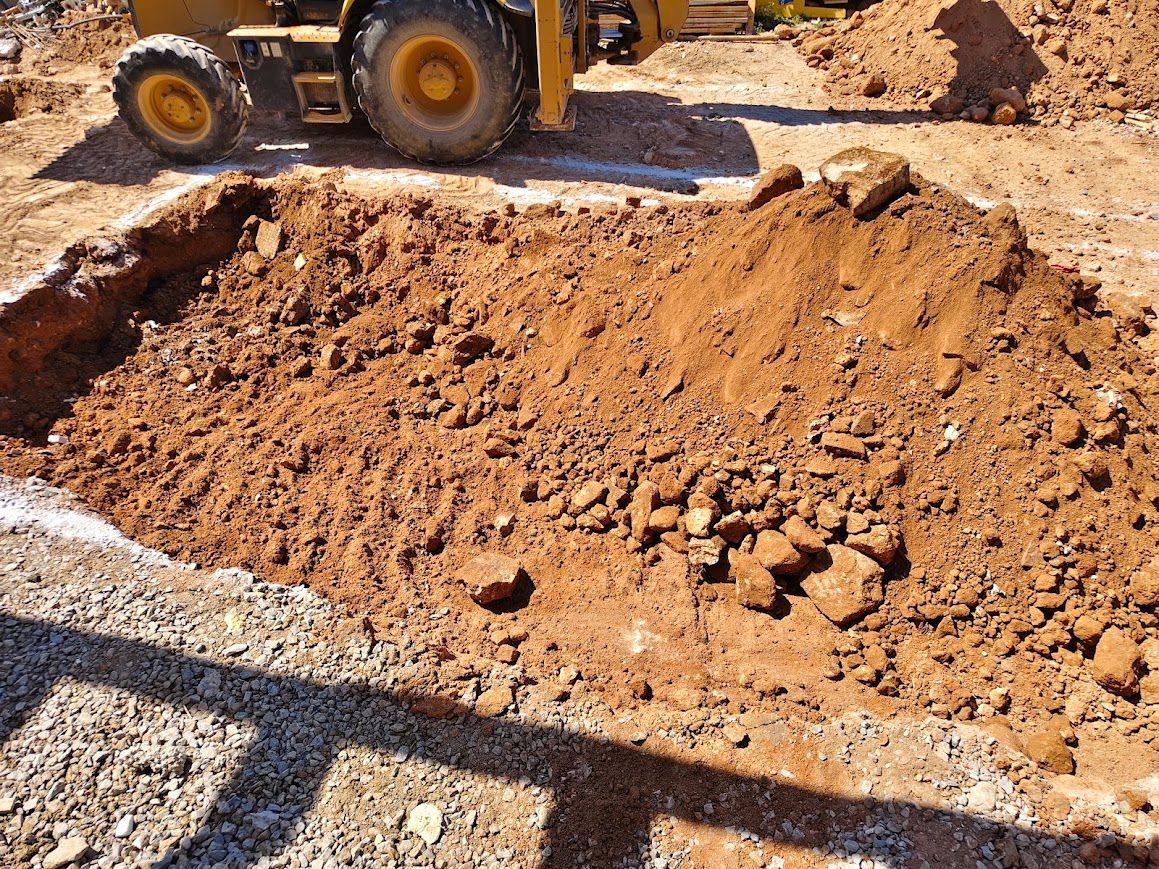 Montón de tierra recién removida en una obra de construcción, con la rueda de una cargadora visible al fondo.