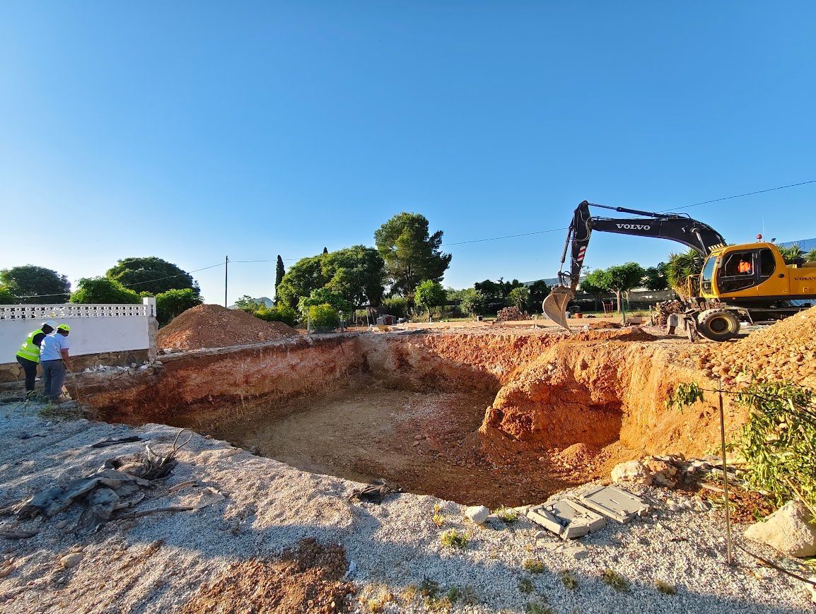 Excavadora cavando una gran fosa de tierra en una obra de construcción bajo un cielo azul despejado.