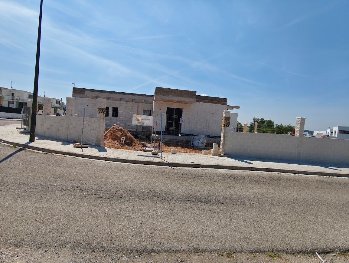 Casa parcialmente demolida junto a una carretera bajo un cielo azul claro, con escombros delante.