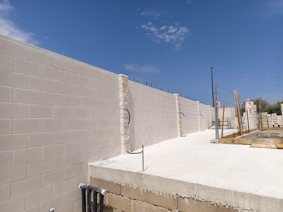 Muro de bloques de cemento parcialmente construido junto a una losa de hormigón blanco bajo un cielo azul.