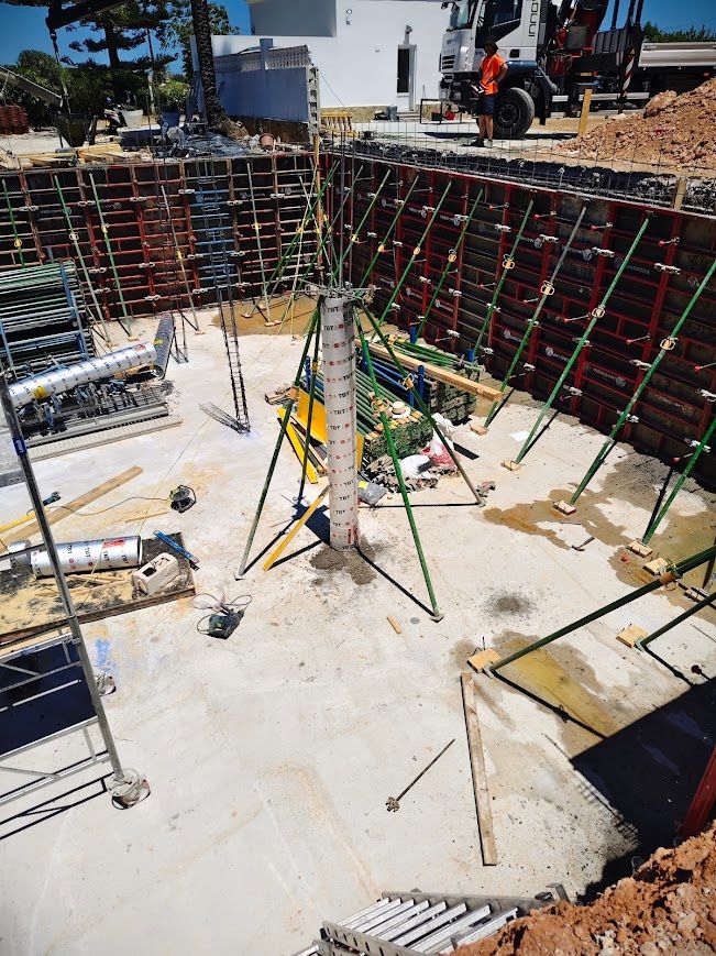 Obra en construcción con trabajadores, muros de barras de refuerzo y una gran fosa de cimentación 