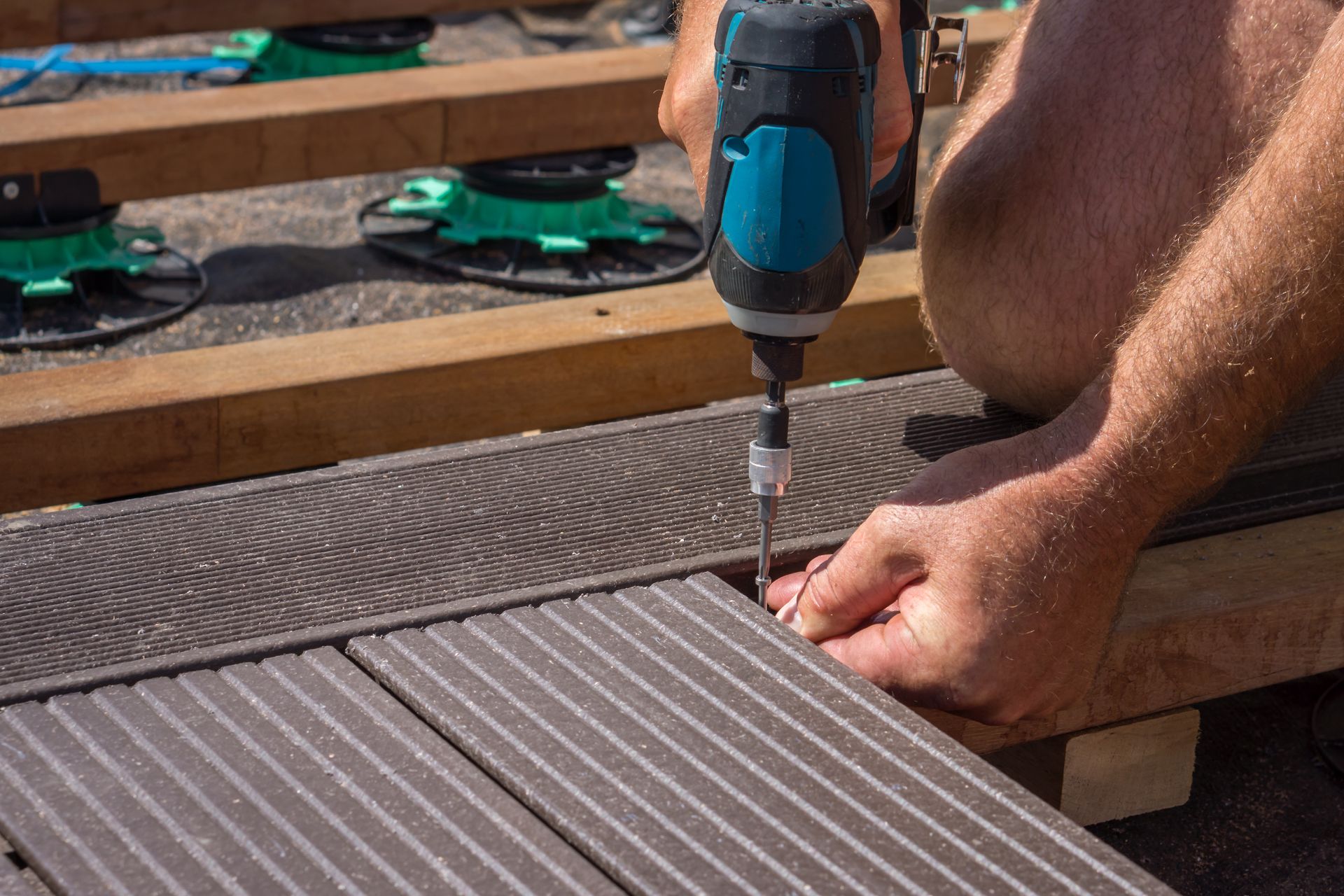 Personne utilisant une perceuse électrique pour installer des planches de terrasse composites sur un cadre de terrasse.