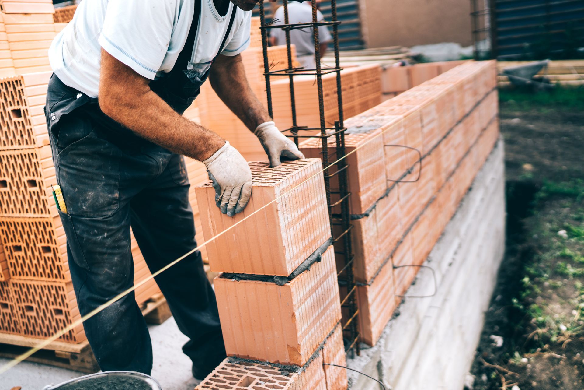 Maçon en salopette, pose de briques, construction d'un mur, en extérieur.