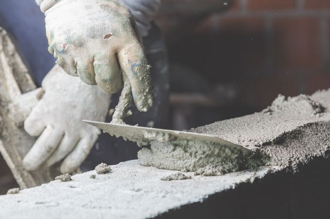 Une personne portant des gants utilise une truelle pour appliquer du ciment sur une surface.