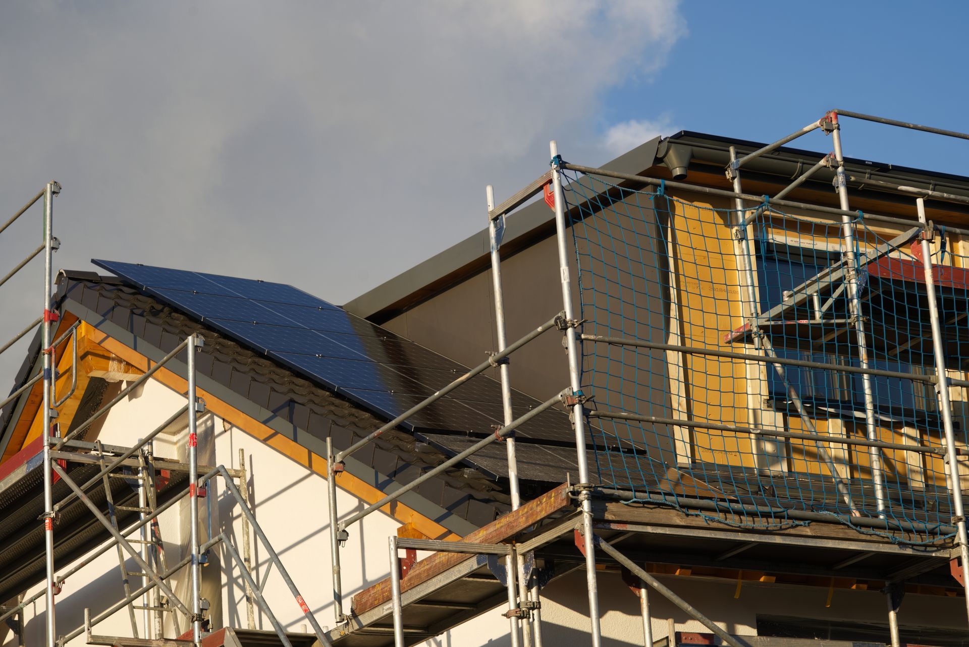 Panneaux solaires sur le toit d'une maison en construction avec échafaudage ; ciel bleu en arrière-plan.