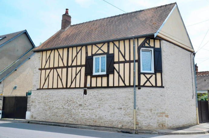 Maison à colombages avec poutres en bois foncé, stuc clair et toit en tuiles rouges.