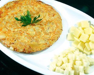 Tortilla española con patatas cortadas en cubitos en un plato blanco, adornada con perejil.