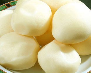 Pila de bollos de color amarillo pálido cocidos al vapor en un plato con un borde con dibujos verdes y negros.