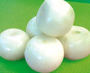 Cinco cebollas blancas peladas apiladas sobre una superficie verde.