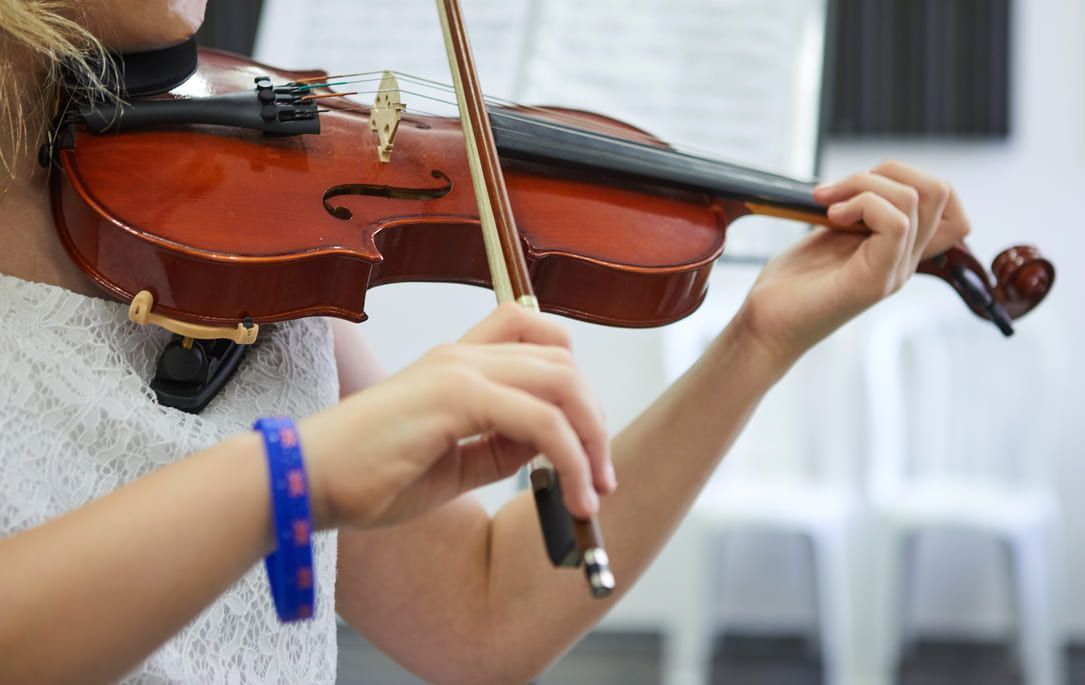Persona tocando el violín en interiores, con las manos en el arco y el diapasón.