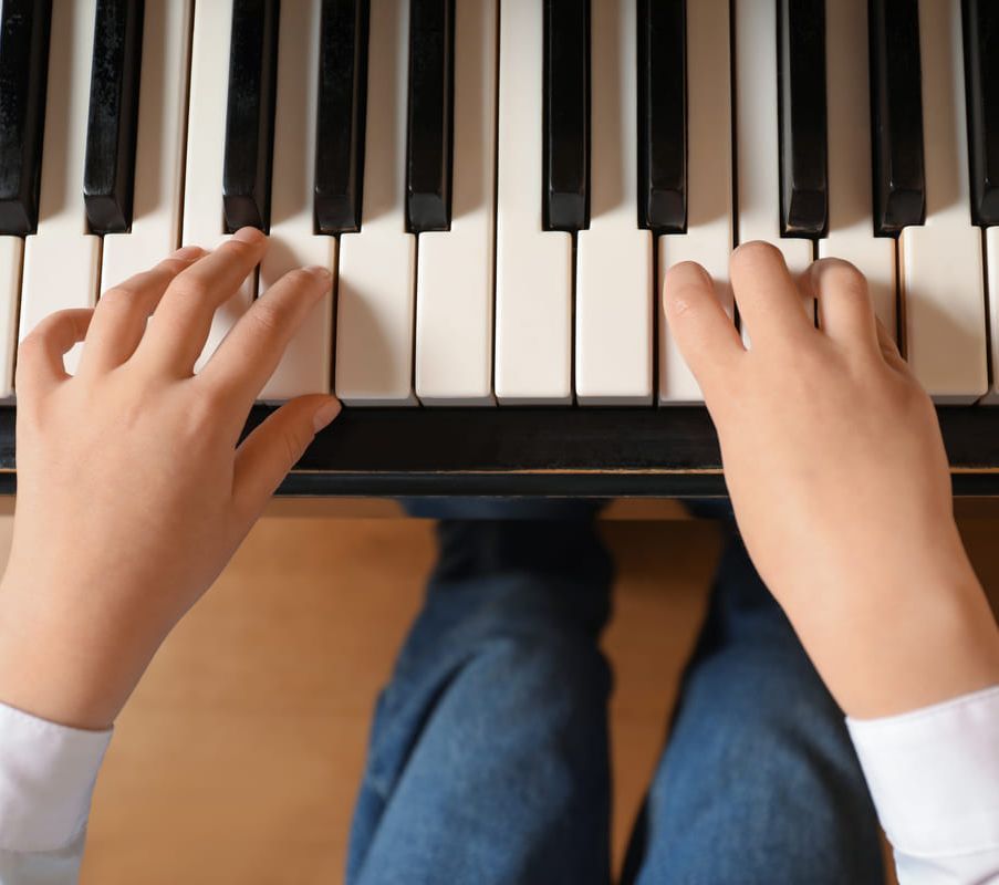 Manos tocando un teclado de piano desde arriba, con unos vaqueros azules visibles debajo.