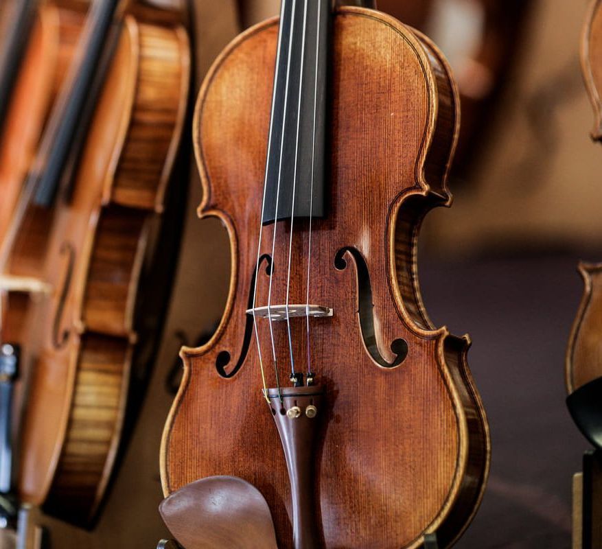 Primer plano de un violín de madera colgado entre otros instrumentos de cuerda en una tienda.