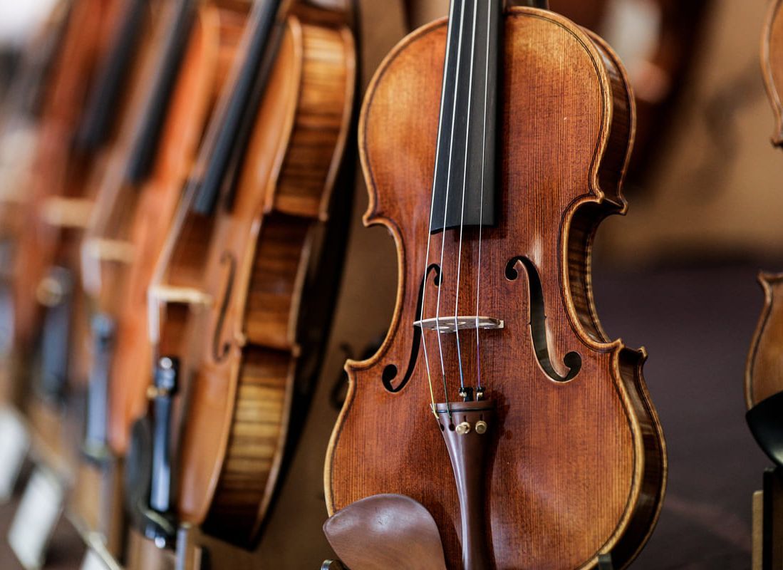 Primer plano de una hilera de violines de madera pulida expuestos, con un violín centrado al frente.