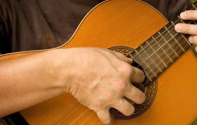 Primer plano de unas manos tocando una guitarra acústica marrón.