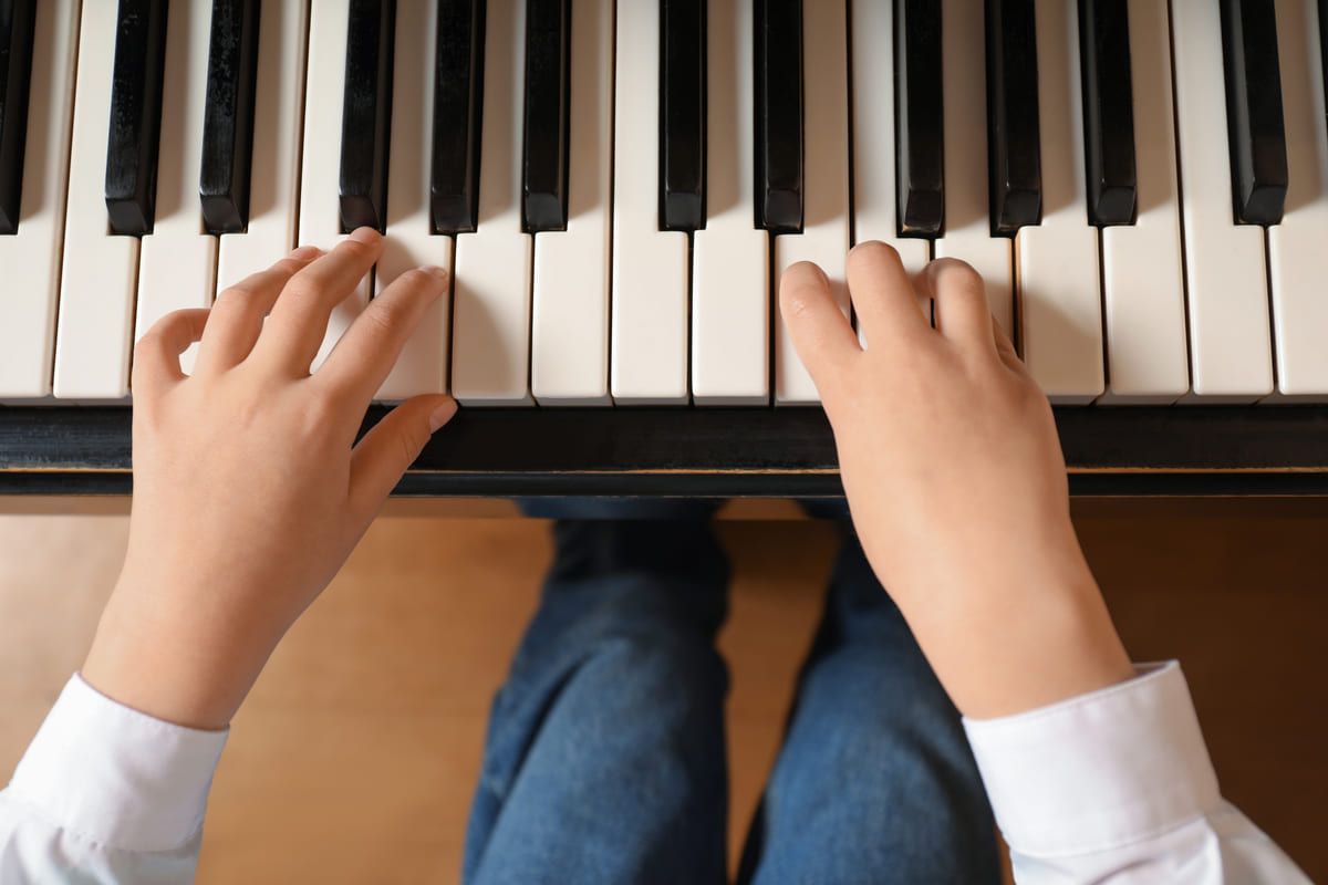 Manos tocando las teclas de un piano desde arriba, con teclas blancas y negras y vaqueros visibles.