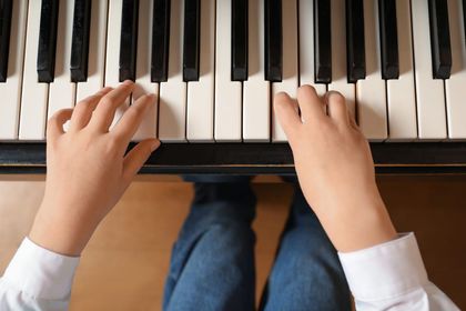 Manos tocando las teclas de un piano desde arriba, con teclas blancas y negras y vaqueros visibles.