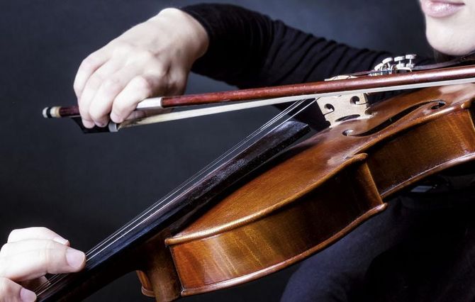 Primer plano de una persona tocando el violín con un arco sobre un fondo oscuro.