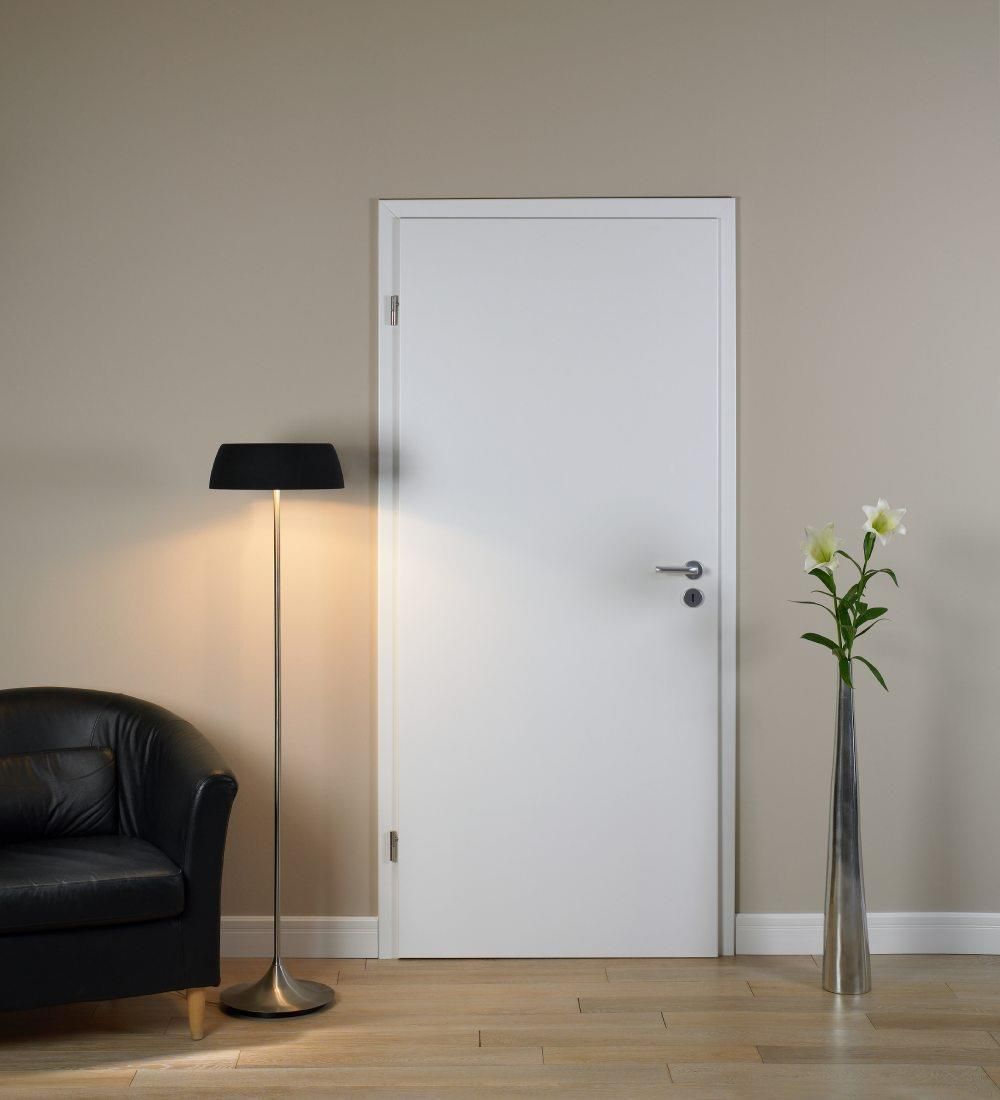 Ein Wohnzimmer mit einer weißen Tür, einem schwarzen Stuhl, einer Lampe und einer Vase mit Blumen