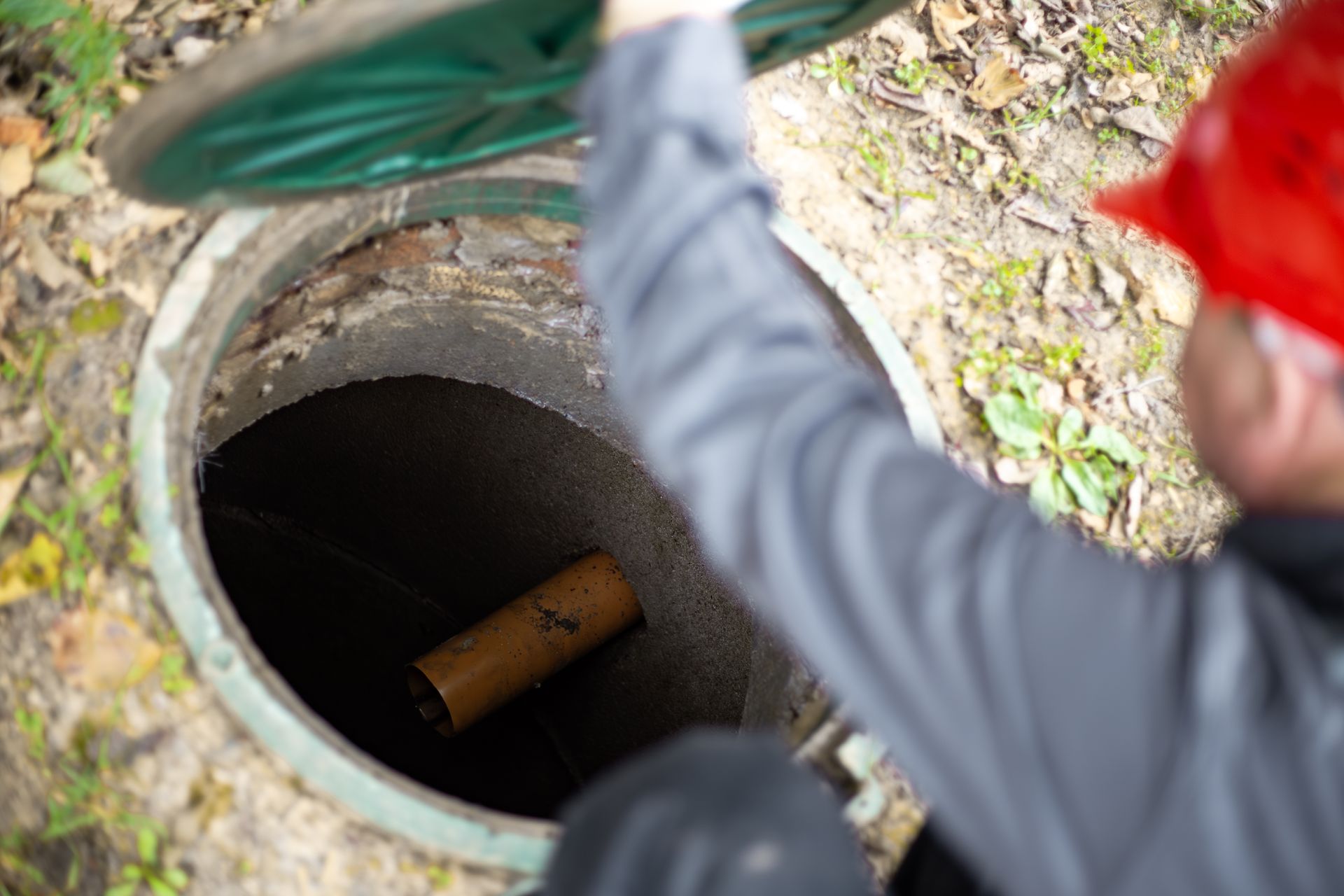 Un ouvrier au casque rouge inspecte une fosse septique.