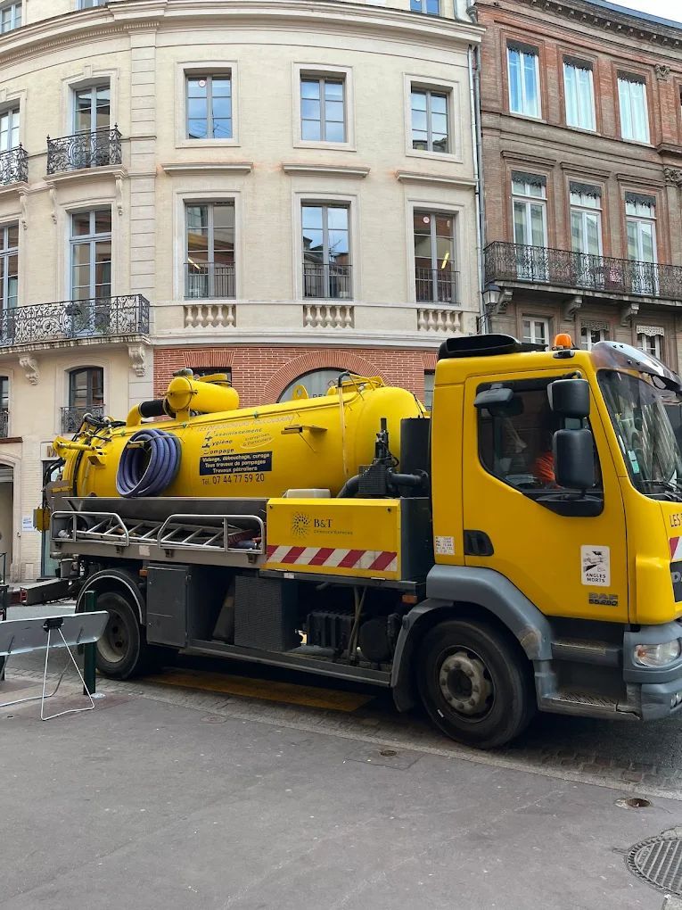 Camion hydrocureur jaune stationné dans une rue du centre-ville de Toulouse.