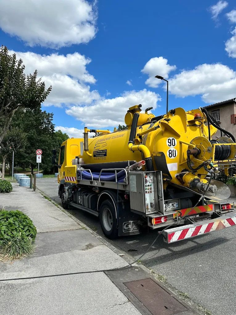 Camion d'assainissement et de curage, stationné dans une rue résidentielle, sous un ciel bleu.