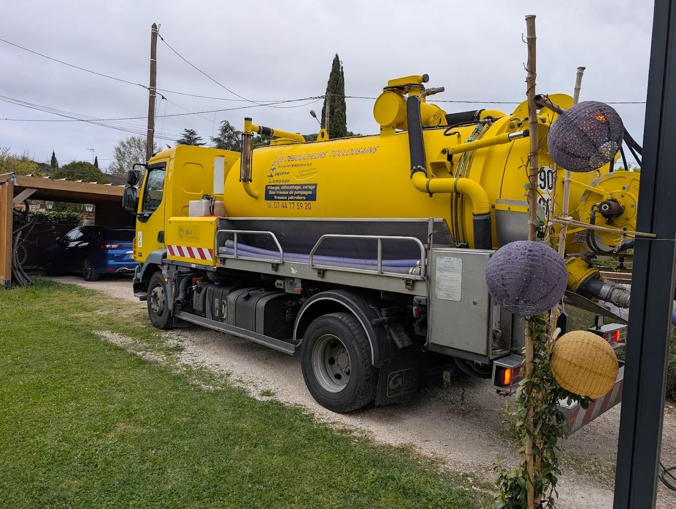 Camion hydrocureur jaune de l'entreprise Les Déboucheurs Toulousains, garé à côté d'une allée herbeuse.