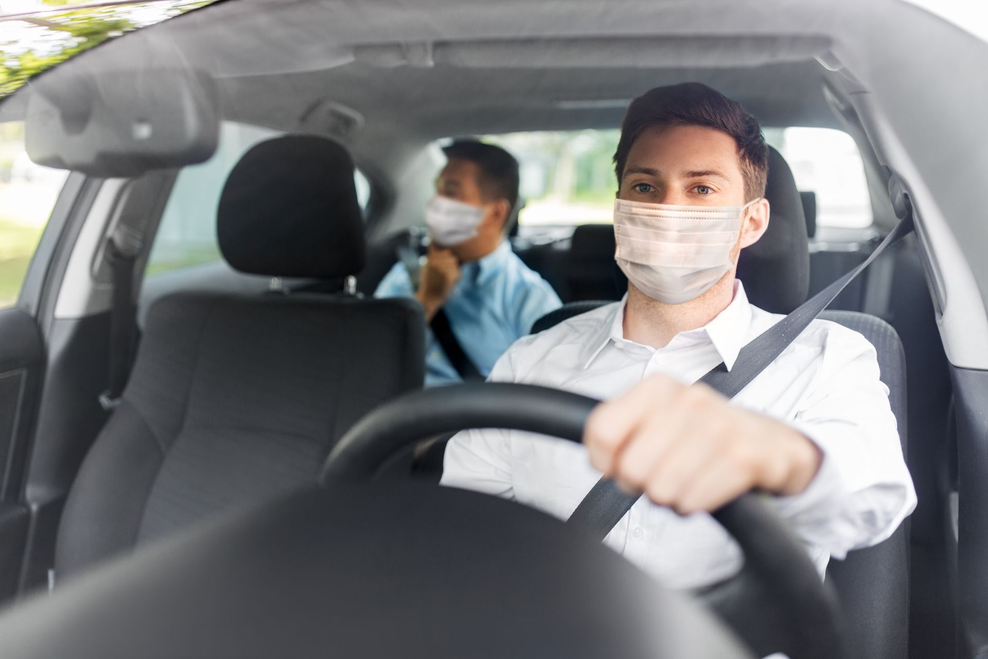 Deux personnes portant des masques dans une voiture, l'une au volant et l'autre assise à l'arrière.