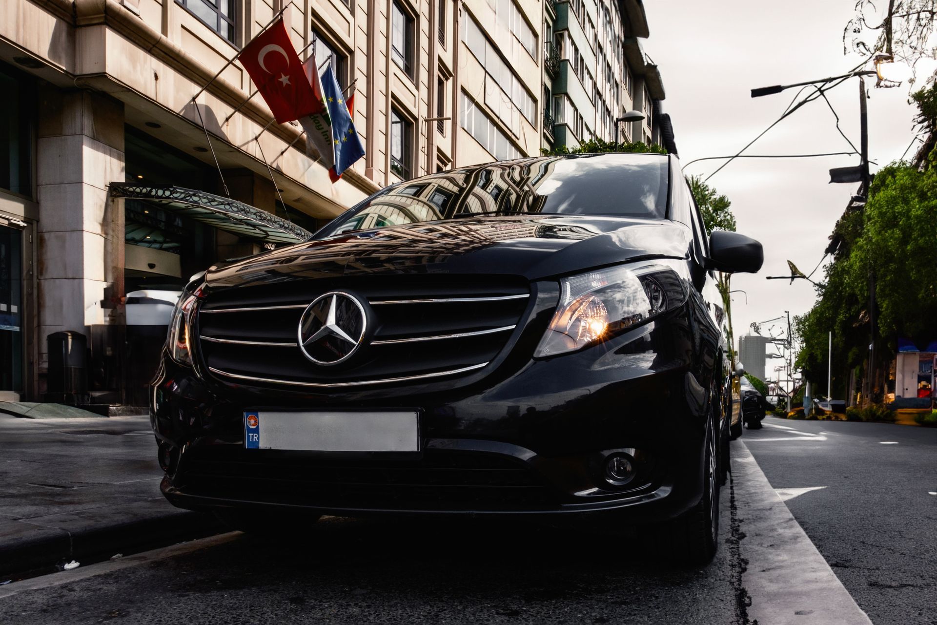 Fourgonnette Mercedes noire garée dans une rue de la ville, le long d'un trottoir, vue de face en plein jour.