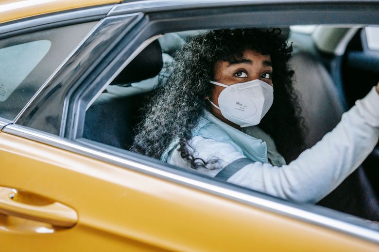Une personne dans une voiture jaune, portant un masque et regardant par la fenêtre.
