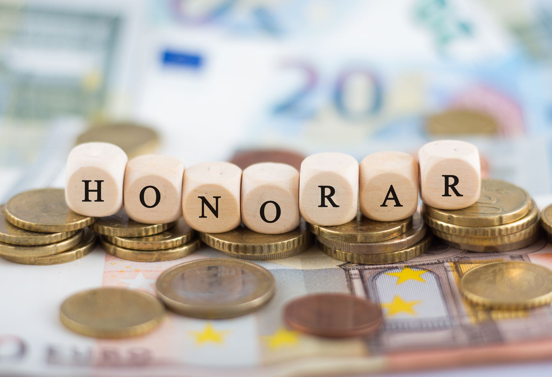 das Wort Honorar steht auf Holzwürfeln auf einem Stapel Münzen und Banknoten .