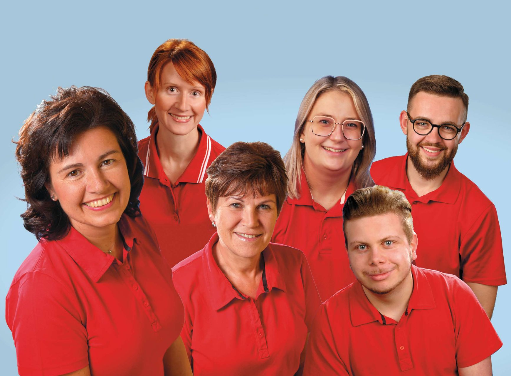 Gruppe von sechs Personen in roten Poloshirts, die vor hellblauem Hintergrund lächeln.