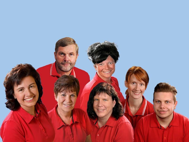 Gruppe von sieben Personen in roten Hemden vor blauem Hintergrund, die in die Kamera lächeln.